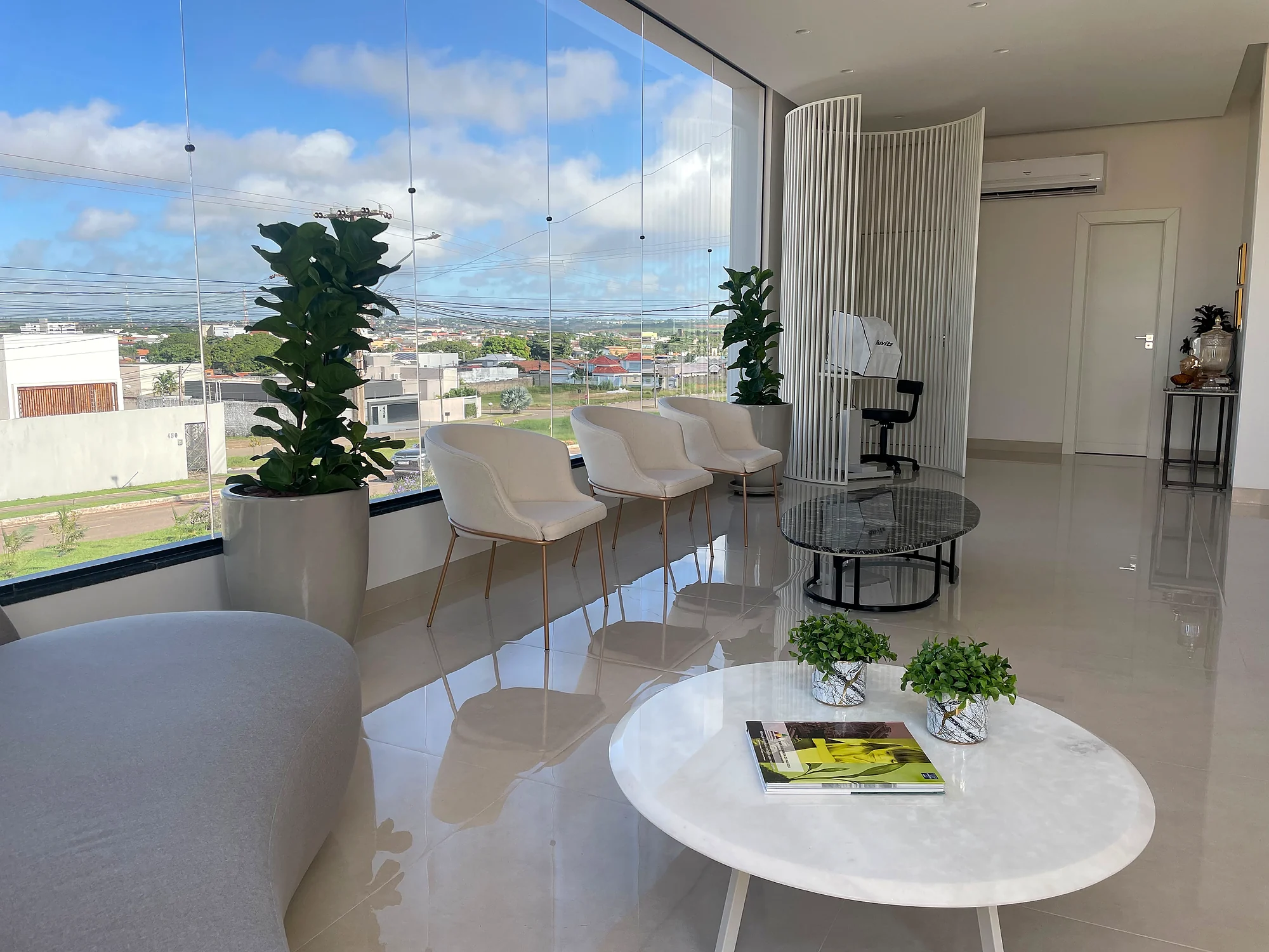 Sala de espera ampla, com poltronas, mesa de centro e janela panorâmica
