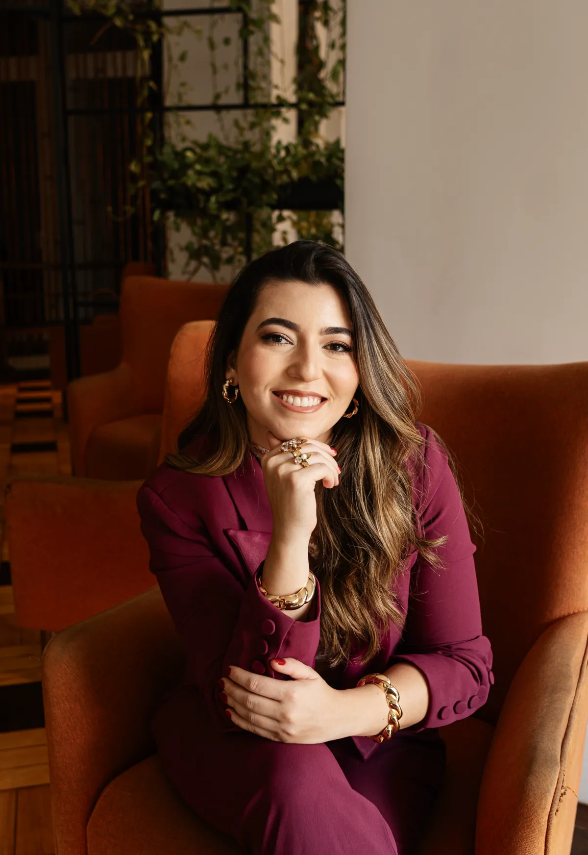 Dra. Nabila Demachki sentada em uma poltrona laranja, com a mão no queixo